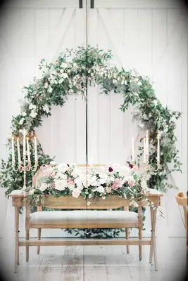 wooden wedding sweetheart table set against a backdrop of a life-sized greenery wreath hanging on white barn doors
