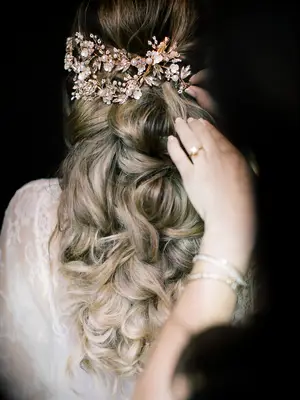 half-up wedding hairstyle with voluminous curls and rose gold rhinestone hair accessories