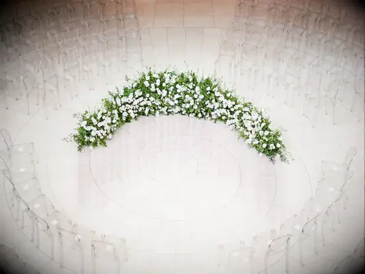 aerial view of indoor wedding ceremony with ghost chairs arranged in a circular shape and floral arch at the center