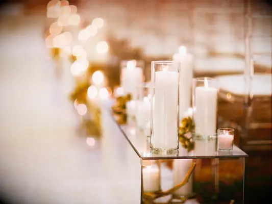 wedding ceremony aisle decor with white pillar candles in glass vases on top of a mirrored box 