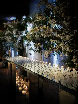 folded white wedding escort cards arranged on a mirrored tabletop with oversized white floral arrangements and votive candles