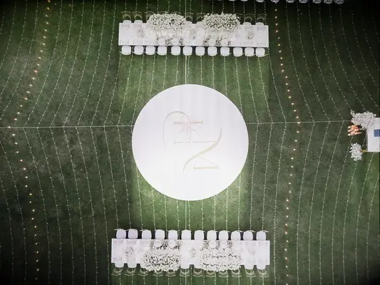 aerial photo of outdoor wedding reception with round monogrammed dance floor under a canopy of string lights