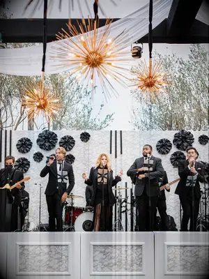 live band performs on stage at luxury wedding with modern sunburst chandeliers and custom flower wall decorating the venue
