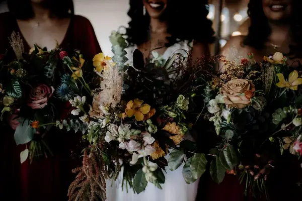 A bride and her bridesmaids smile for the camera, holding breathtaking autumnal bouquets.