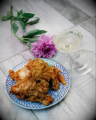A plate of mouthwatering fried chicken sits beside a purple dahlia and a vintage punch glass.