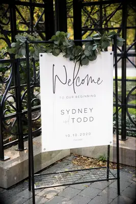 A metal easel holds a welcome sign, adorned with greenery.