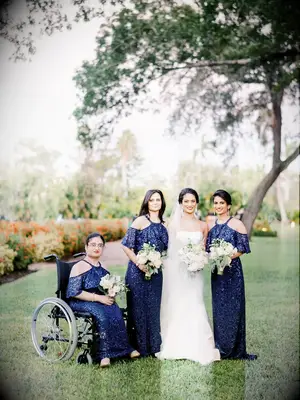 A bride poses with her three bridesmaids, each of whom wears sparkling navy gowns.
