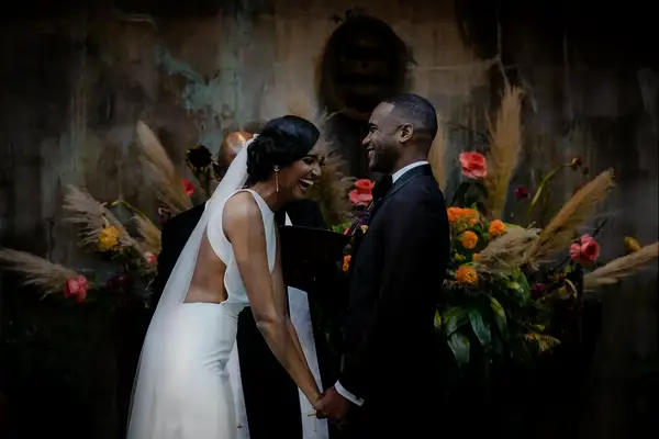 The happy couple laugh together in front of stunning floral arrangements of pampas grass.