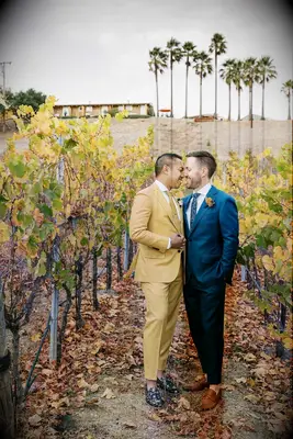 A pair of grooms lean in for a kiss among the yellows and green of an autumnal winery.