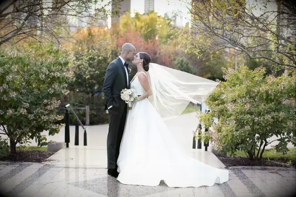 A couple leans in for a kiss among the greenery at their favorite park.