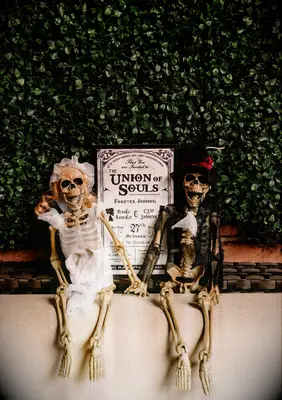 A spooky Halloween-inspired wedding welcome sign, complemented by a pair of skeletons dressed for the occasion.