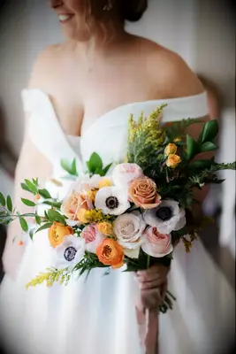 A bride holds this gorgeous autumnal bouquet with panda anemones and pink and orange roses.