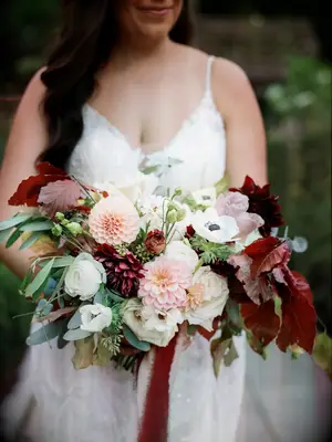 A bride holds a burgeoning bouquet of warm wine colors.