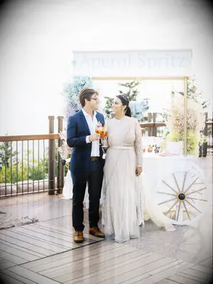 bride and groom standing in front of cocktail cart with sign that says aperol spritz
