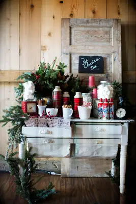 DIY hot chocolate bar on vintage dresser with greenery, chalkboard sign and red plaid thermoses 