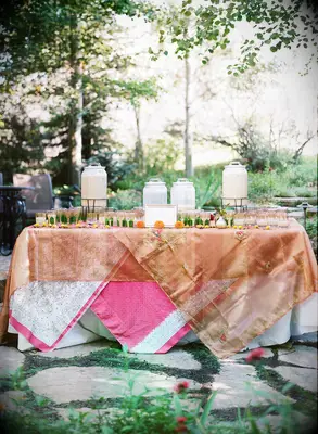 outdoor wedding drink station idea with colorful layered tablecloths and chai tea in dispensers