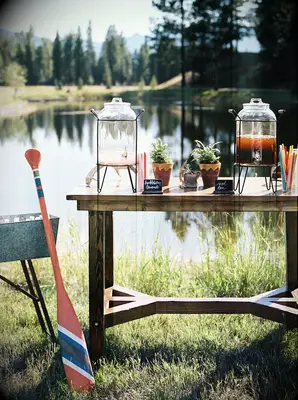 outdoor wedding drink station idea with glass dispensers of iced tea and lemonade on a wooden table in front of a lake