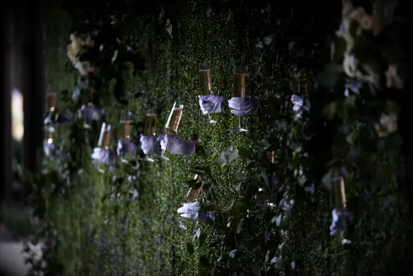 greenery wall with gloved servers passing champagne through windows