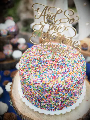wedding cake with rainbow sprinkles and gold cake topper that says 