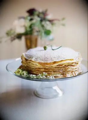 A plate of French crepes stacked on top of each other and topped with powdered sugar. 