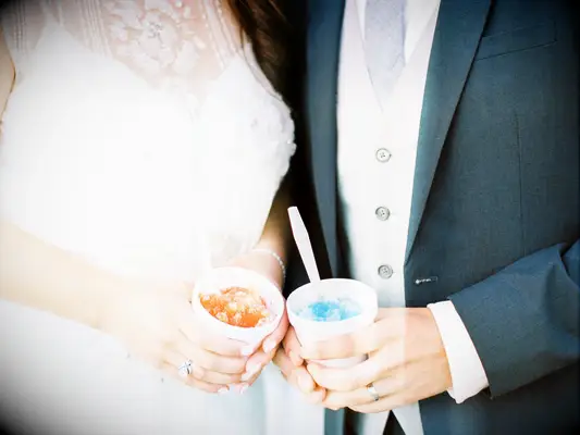 Couple holds cups of colorful snow cones in hand. 