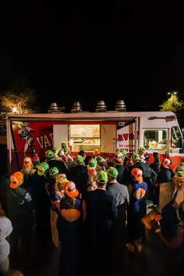 Crowd stands outside a food truck. 