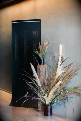 modern wedding seating chart display with table assignments written on black cloth backdrop accented with large pampas grass and greenery arrangements