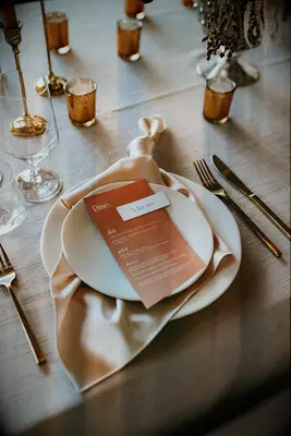 wedding place setting showcasing winter wedding colors with cream textured linen, white plates, gold flatware, beige satin napkin and rosy pink wedding menu card