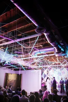 indoor wedding ceremony at industrial venue with colorful neon light bars hanging from the ceiling