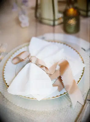 elegant wedding place setting with gold-rimmed china and blush pink ribbon tied in a bow around white cloth napkin