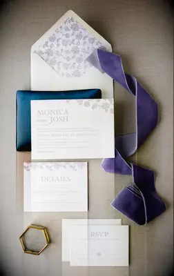 wedding invitation flatlay with pale purple embossed invitations and purple floral print envelope liner