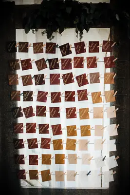wedding escort card display featuring square cards in ombre dark to light brown colors attached to ropes with clothespins
