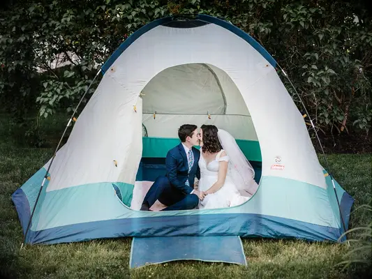 Bride and groom sitting in tent at camp-inspired outdoor summer backyard wedding