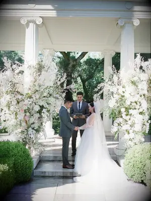 Bride and groom reciting vows in front of lavish white floral installations at summer wedding