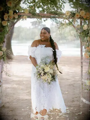 Bride holding bouquet of yellow flowers under yellow floral ceremony arch at outdoor summer wedding