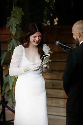 Bride in Modern Gown Getting Emotional Reading Vows From Book at Casual Ceremony