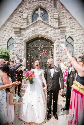 Couple leave their wedding ceremony while guests throw flower petals. 