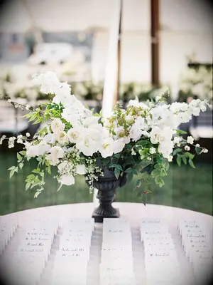 wedding escort card display with white and greenery centerpiece in black urn vase
