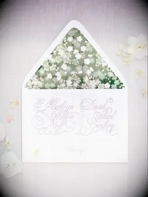 formal classic wedding invitation with embossed calligraphy against white background and green floral print envelope liner