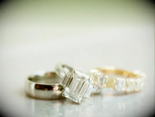close-up of three-stone emerald cut engagement ring on silver band with yellow gold diamond wedding band and groom