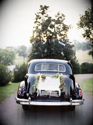 view of newlywed couple kissing through the back window of black vintage car decorated with 