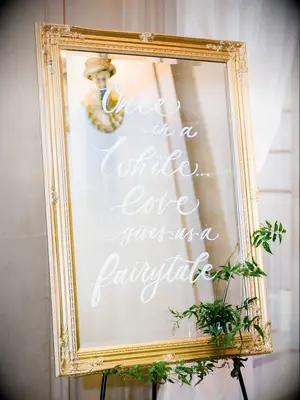 mirror wedding sign in gold frame and quote written in white calligraphy: 