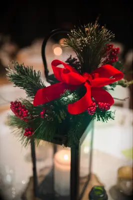 Lantern with candle in it, decorated with pine, red ribbon, and pine cones. 