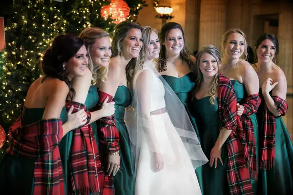 Bridesmaids wearing red plaid shawls while posing with the bride.