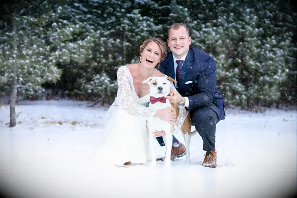Bride and groom smiling with their pet wearing a red bow tie.