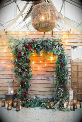 Lush green and red wedding ceremony arch. 
