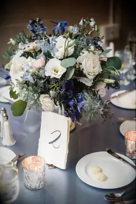 low wedding centerpiece with blue delphinium, white roses, lisianthus and greenery