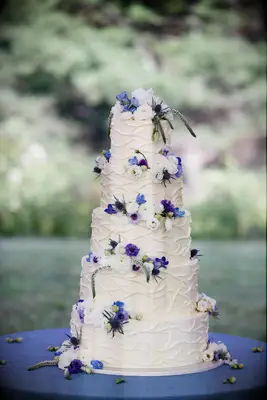five tier white wedding cake decorated with blue, white and purple flowers