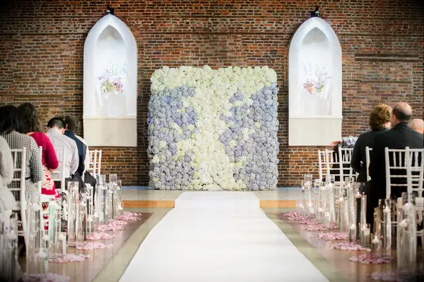 indoor wedding ceremony with flower wall made of blue and white hydrangeas against a brick wall