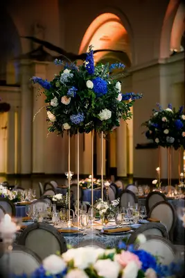 tall wedding centerpiece on gold base with blue hydrangeas, blush roses, blue delphinium and greenery